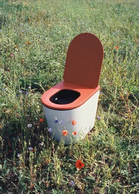 White Luna dry toilet with orange seat standing in a meadow of poppies and cornflowers